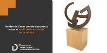 Imagen del premio. Una escultura abstracta y circular de bronce sobre un soporte cuadrado de madera clara.